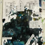 A sheet of paper with paint splatters covers printed tables and charts.